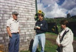 Three people talking beside a farm building, one holding a notebook.