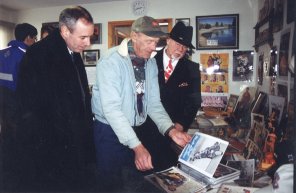 Two men indoors leaning over a table of old photographs.