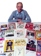 A man standing indoors beside shelves and framed hockey memorabilia.