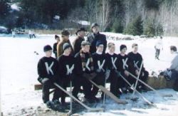 A school team group photograph taken outdoors on ice, players kneeling in front and adults standing behind.